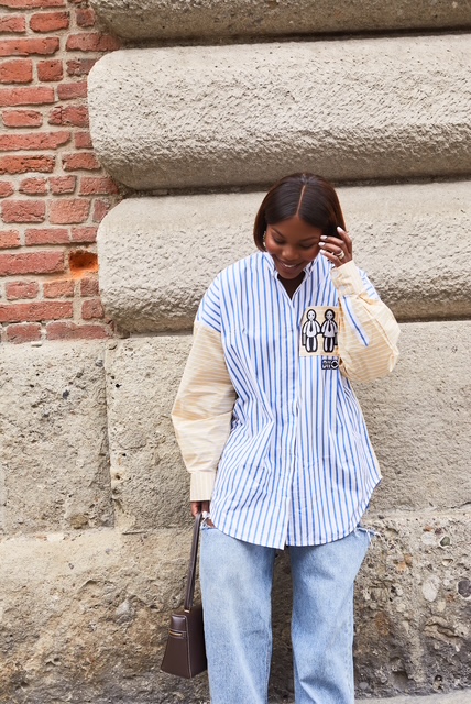 Sacha Okoh in a blue striped shirt and jeans beside a stone wall