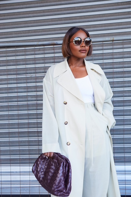 Sacha Okoh wearing a white coat and sunglasses with a woven handbag